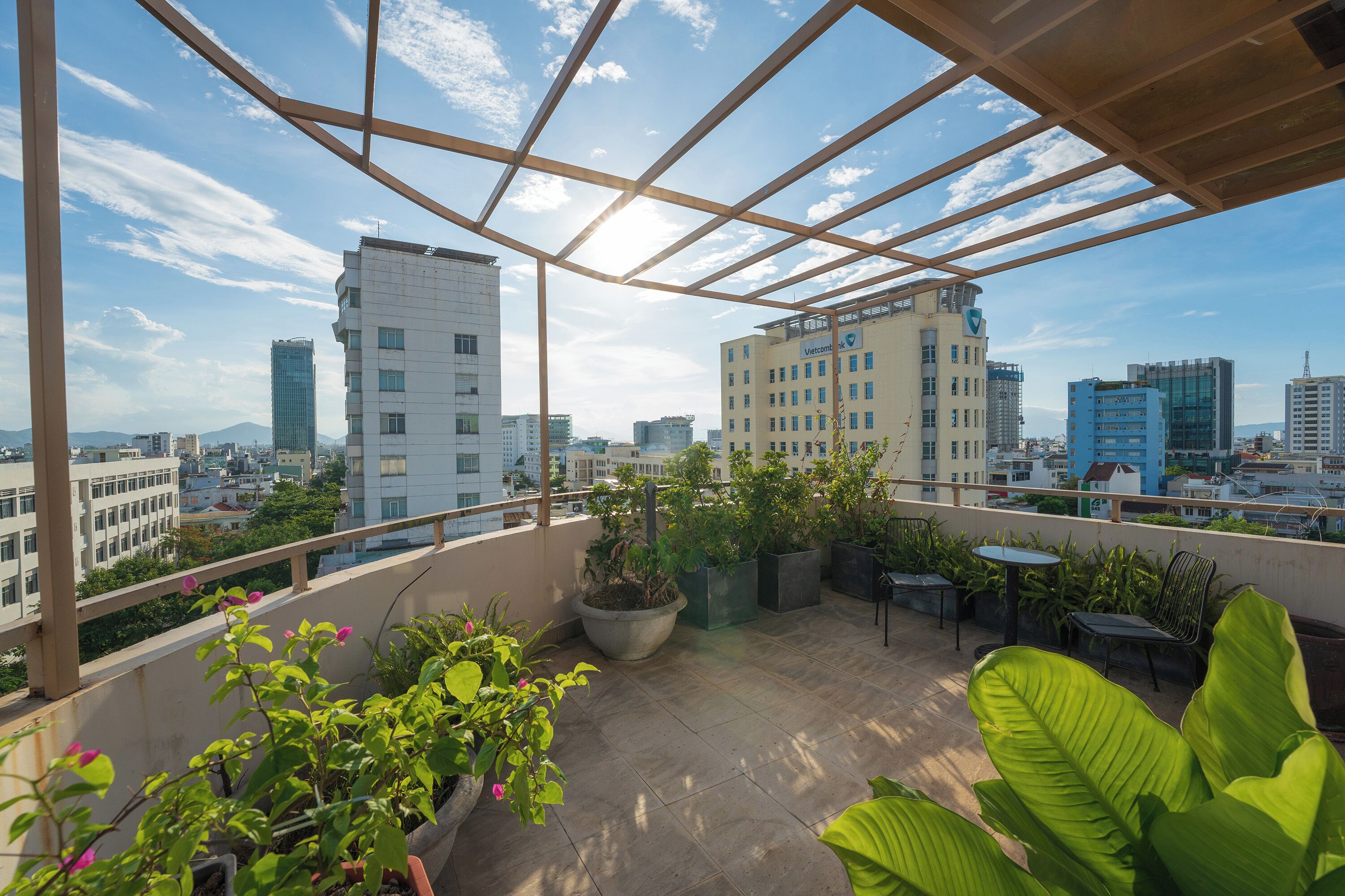 A rooftop terrace with potted plants, outdoor furniture, and a city view.