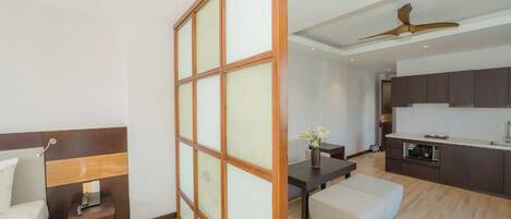 A modern apartment with a wooden-framed sliding door, a dining area with a table and chairs, a kitchenette, and a bed with a headboard.