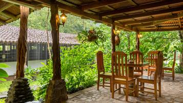 Un patio techado al aire libre con suelo de piedra, sillas y mesas de madera.