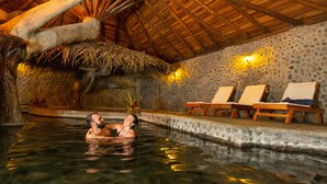A couple in a clear indoor pool with lounge chairs and a stone wall. - Rancho Margot (Tronadora)