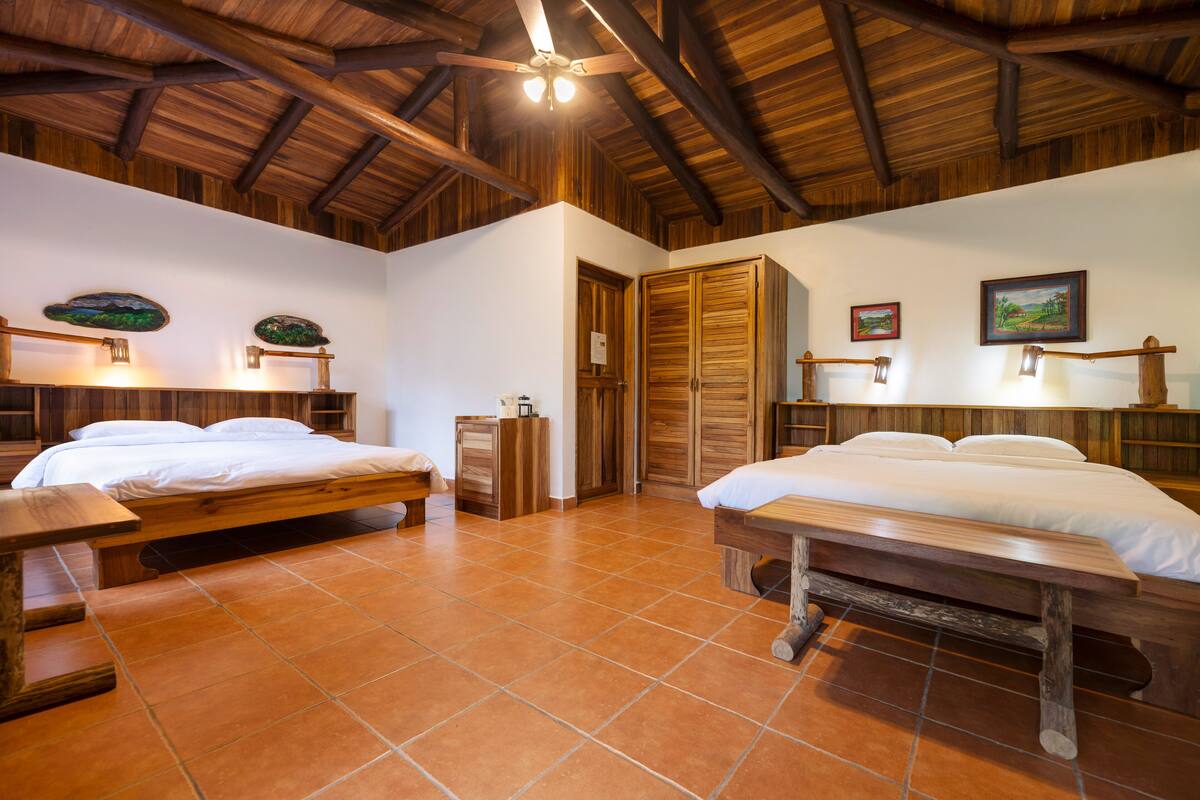 A room with two wooden beds, a wooden bench, a wooden table, and a ceiling fan.