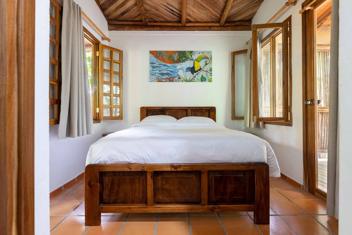 A wooden bed in a room with a tiled floor and a painting on the wall.