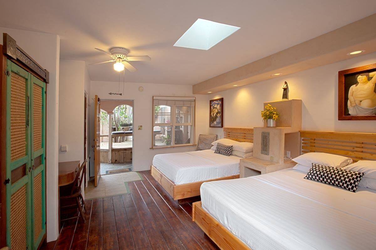 A hotel room with two beds, a ceiling fan, a skylight, a statue, and a painting.