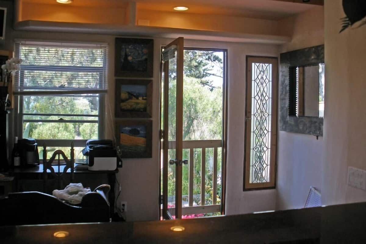 A room with a dining area, a large window with blinds, a door with a decorative metal grille, and a wall-mounted artwork.