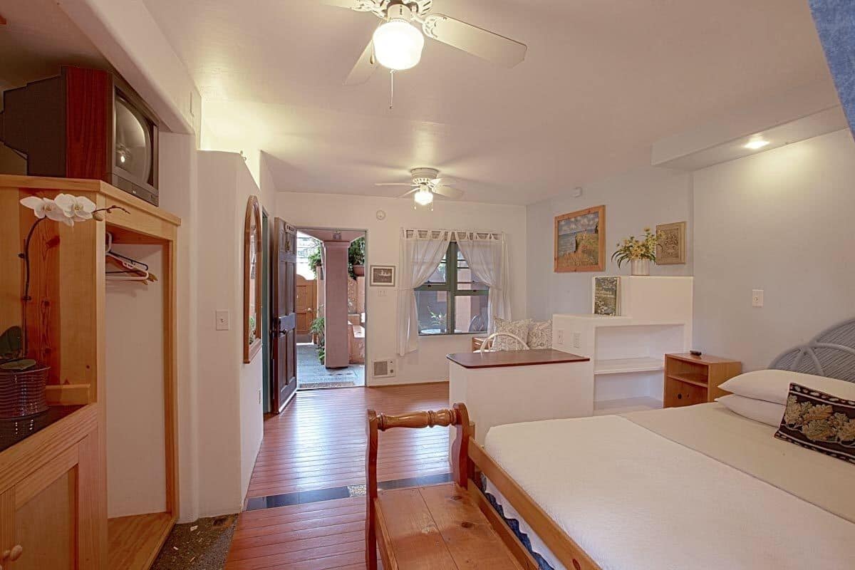 A bedroom with a bed, wooden furniture, a ceiling fan, and a view of the outside.