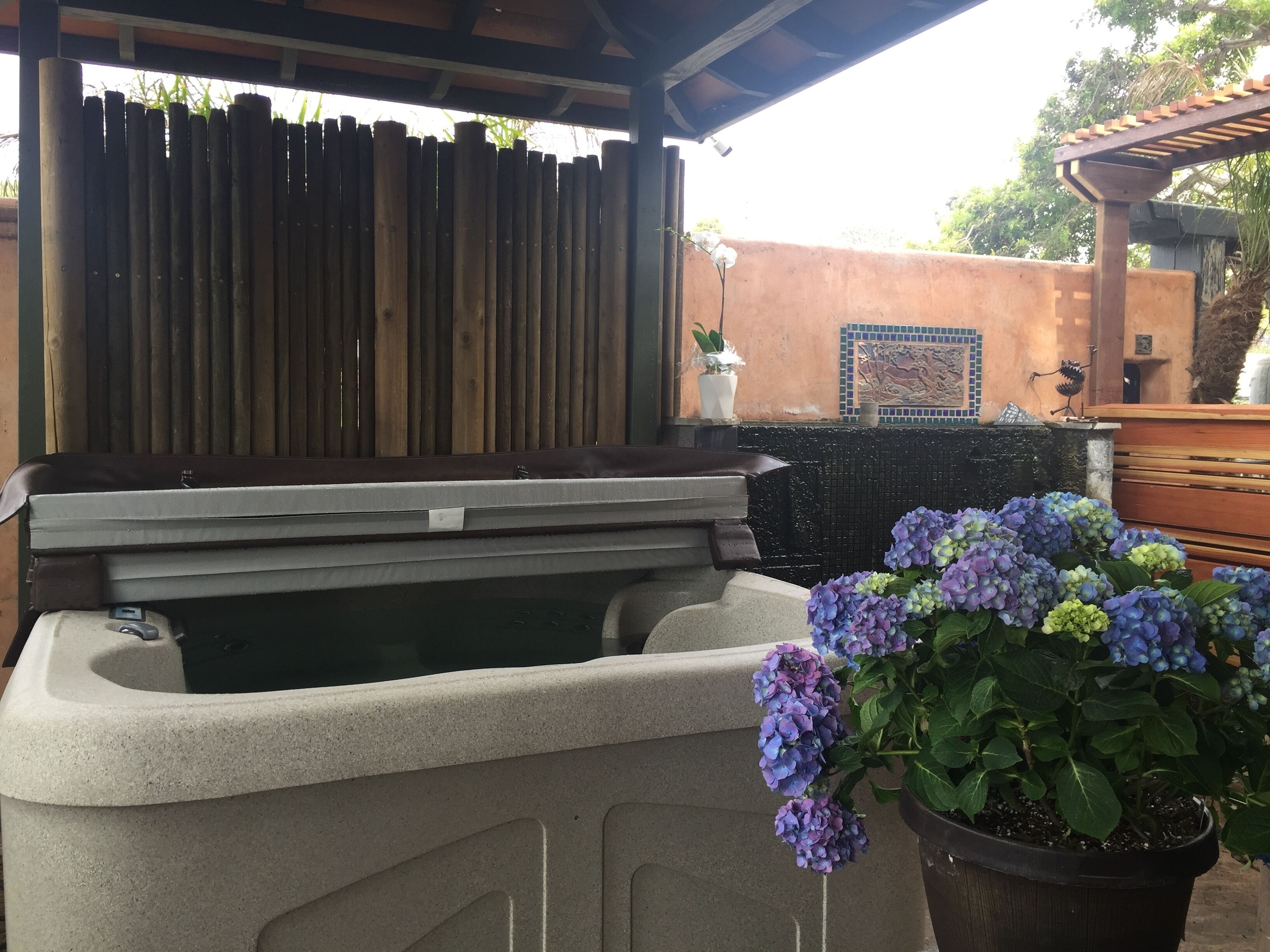 Ein Wellnessbereich mit Whirlpool, Holzzaun und einem Topf mit Hortensien.