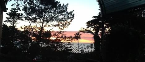 A view through a semi-circular window with a sunset over a body of water, surrounded by trees.
