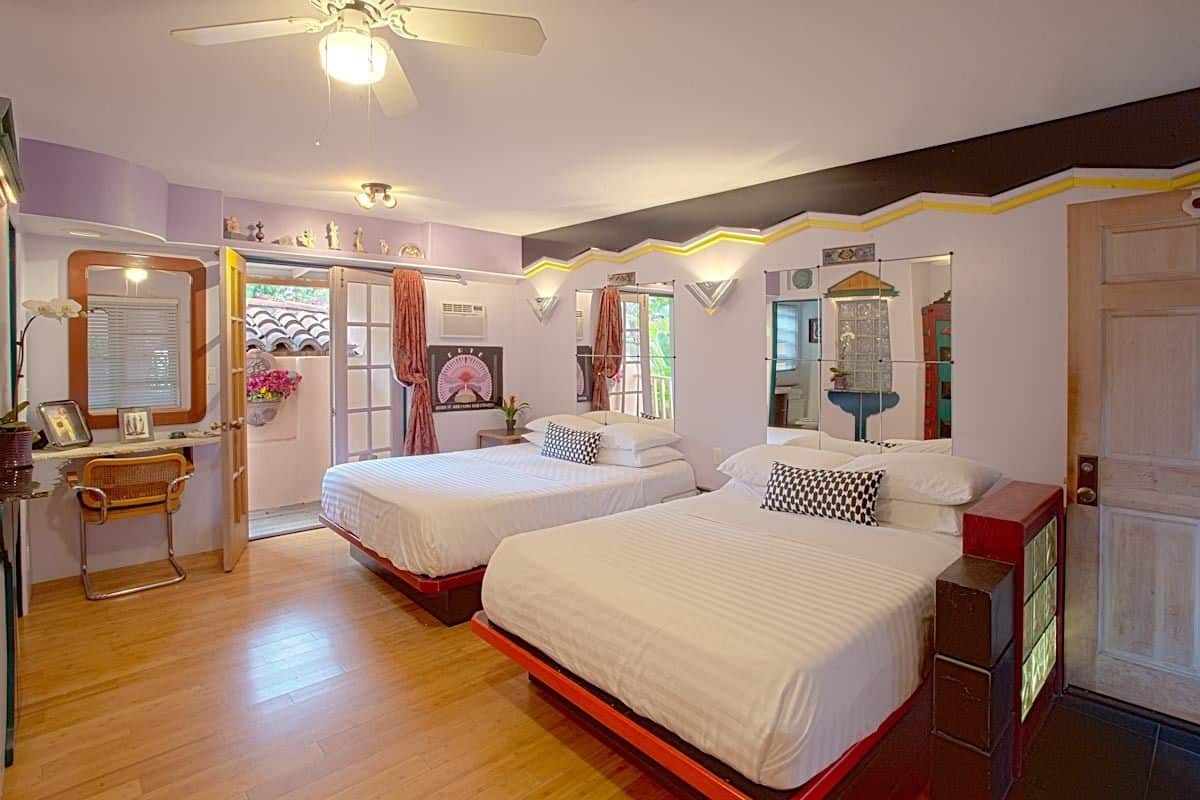 A bedroom with two beds, wooden flooring, a ceiling fan, and a door with a mirror.