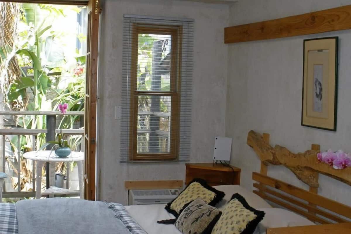 A bedroom with a bed, a wooden headboard, a nightstand, a window, and a view of greenery outside.