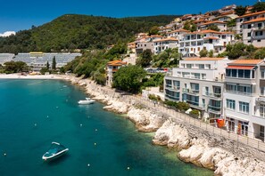 A coastal town with buildings along the waterfront, a rocky shoreline, and a clear blue sea. - Adoral Boutique Hotel (Labin)