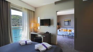 Habitación de hotel con cama, escritorio y televisor. Se ve el mar a través de la ventana.