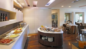 Een modern ontbijtbuffet met diverse gerechten en drankjes, een zithoek met tafels en stoelen, en een schoon, goed verlicht interieur.