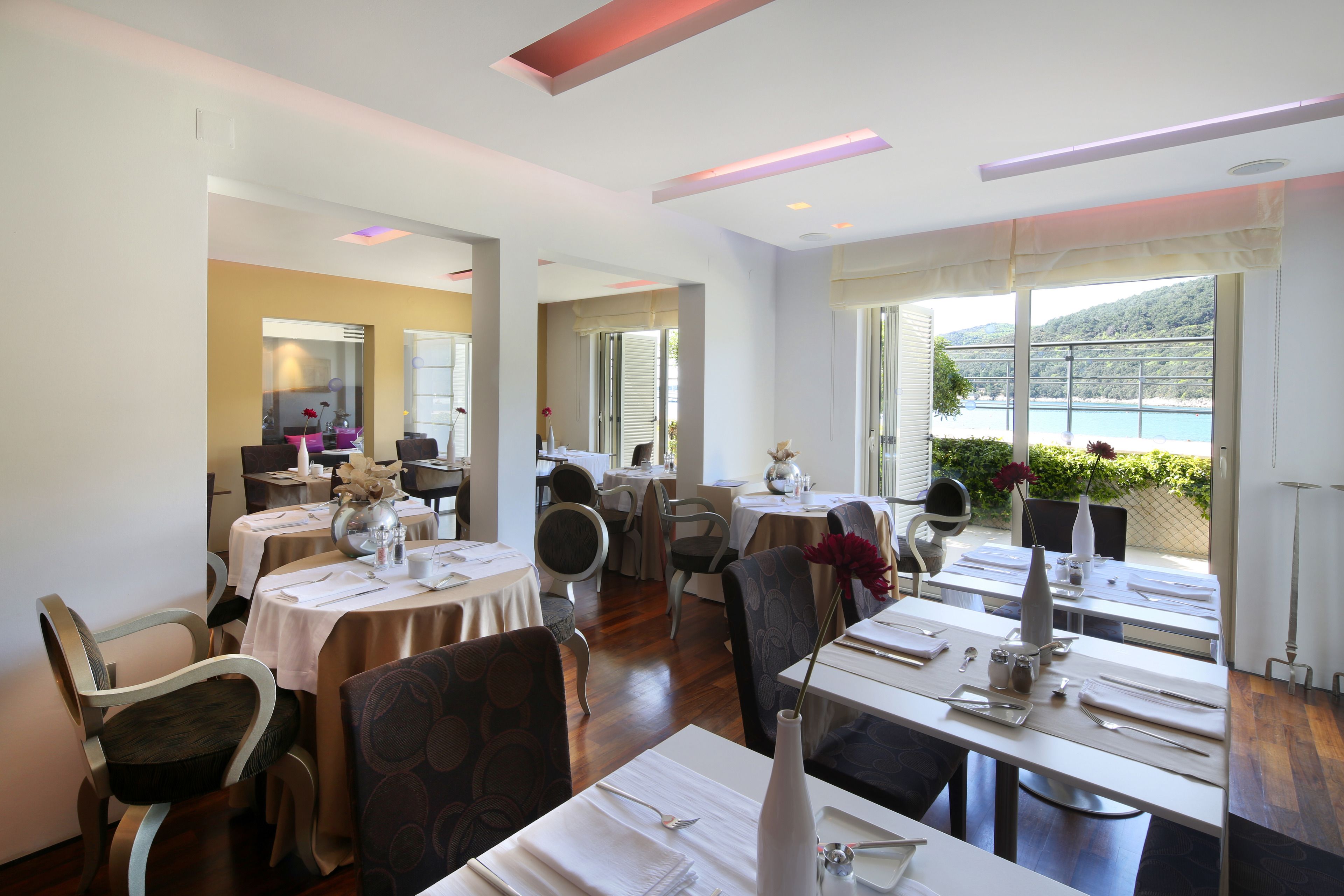 A dining area with tables set for service, large windows with a view of the outdoors, and a modern interior design.