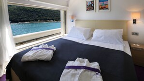 Hotelkamer met een bed, twee kussens, een nachtkastje, een lamp en een raam met uitzicht op water en groen.