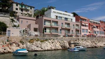 Ein Küstenhaus mit mehreren Balkonen, einer felsigen Küstenlinie und Booten im Wasser.