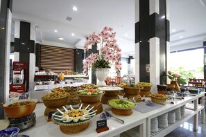 A buffet with various food items and a decorative orchid centerpiece. - SOCO Hotel (Da Nang)