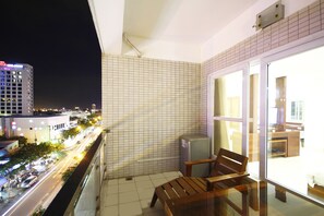 En balkon med flisbeklædt væg, en træbænk og udsigt til en gade i byen om natten.