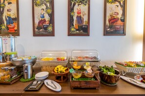A buffet setup with various food items and a wall decorated with traditional paintings.