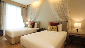 A hotel room with two beds, a nightstand with a lamp, and a window with curtains.