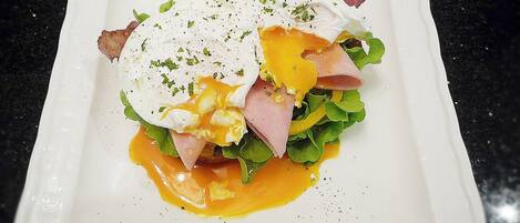 Plato blanco cuadrado con un desayuno que incluye huevos pochados, jamón, queso y verduras, sobre una encimera negra.
