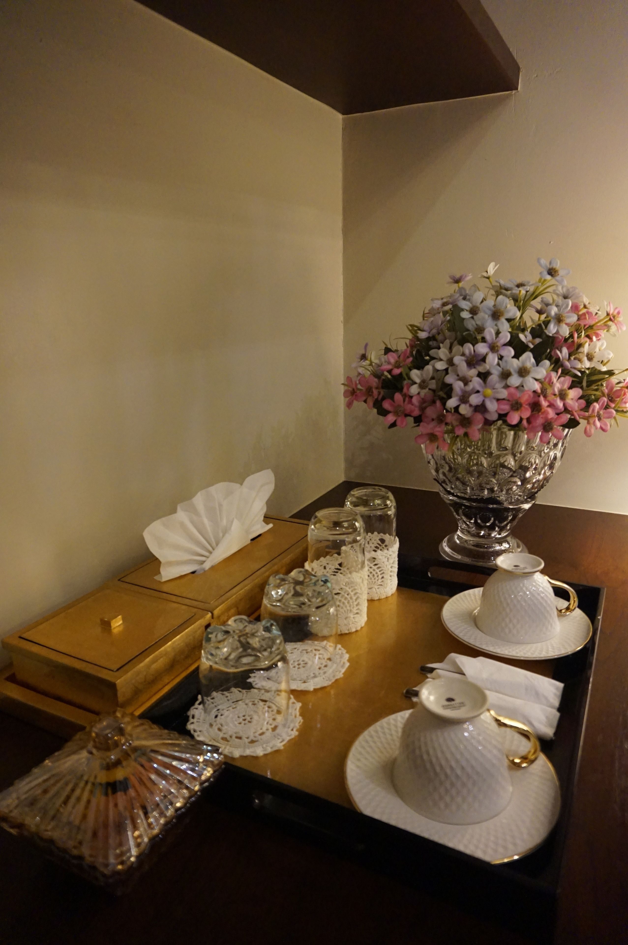 A wooden tray with a white teapot, sugar bowl, and creamer on a table.