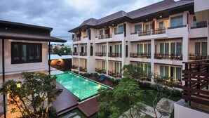 Un hotel de varios pisos con piscina, balcones y abundante vegetación.