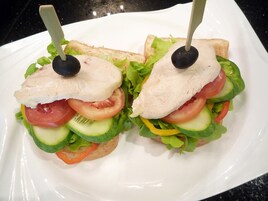 Sanduíche com alface, tomate, pepino e uma azeitona preta sobre um prato branco.