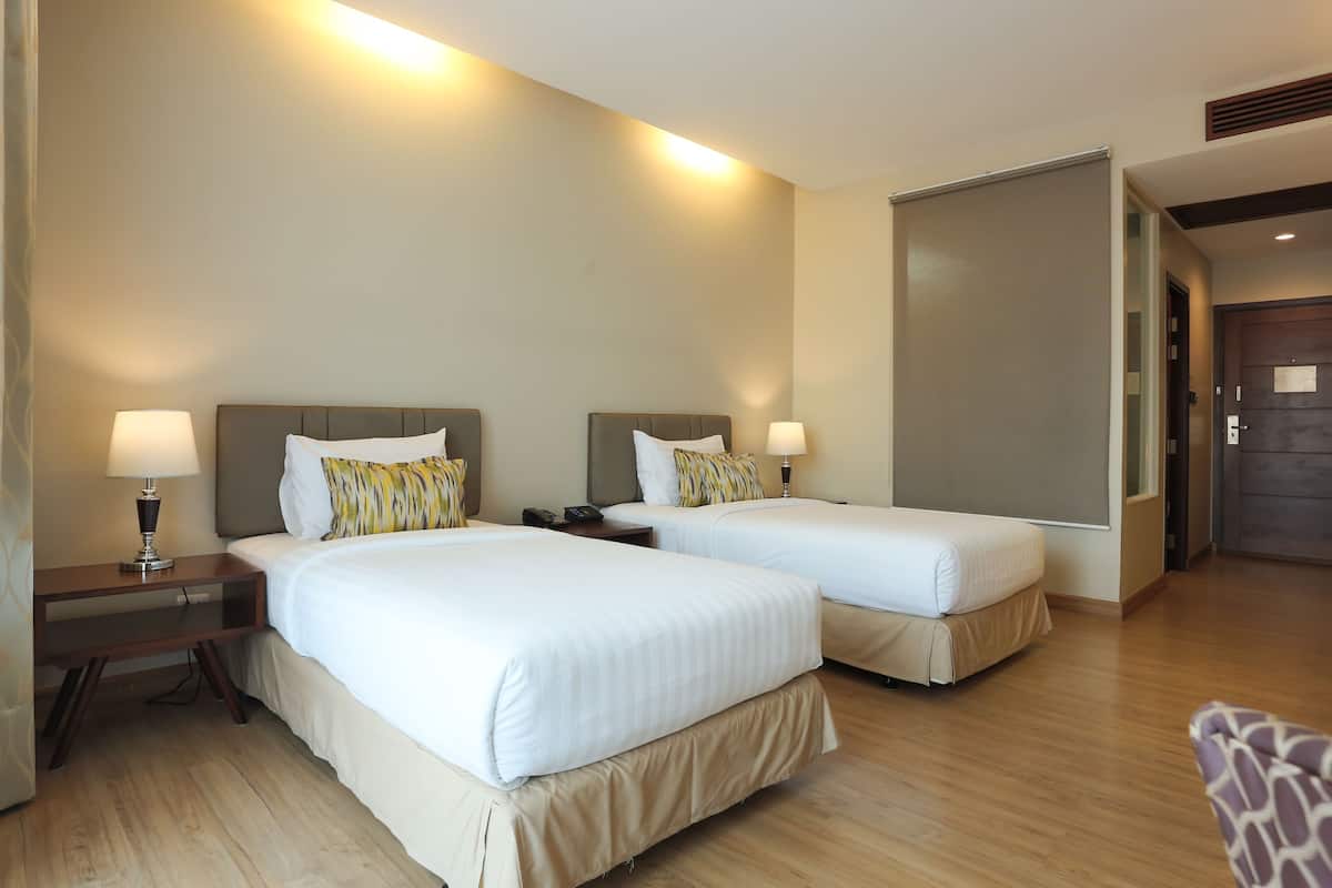 Habitación de hotel con dos camas, cada una con mesita de noche y lámpara, un espejo grande y suelo de madera.