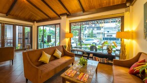 Un hall acogedor con vigas de madera en el techo, un sofá marrón, una mesa de centro con revistas y vista a la calle.