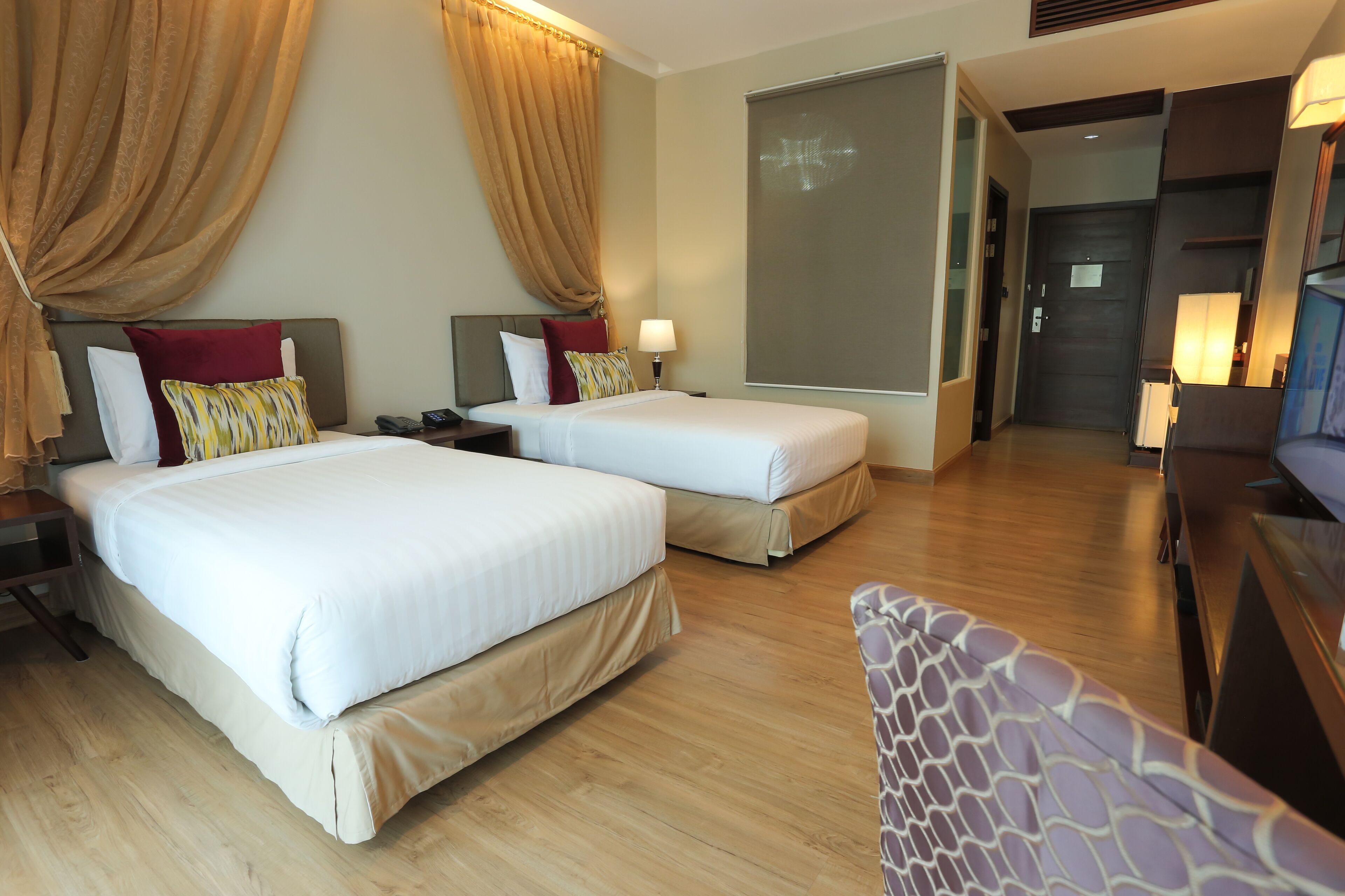 Habitación de hotel con dos camas, televisión, escritorio y un amplio ventanal.