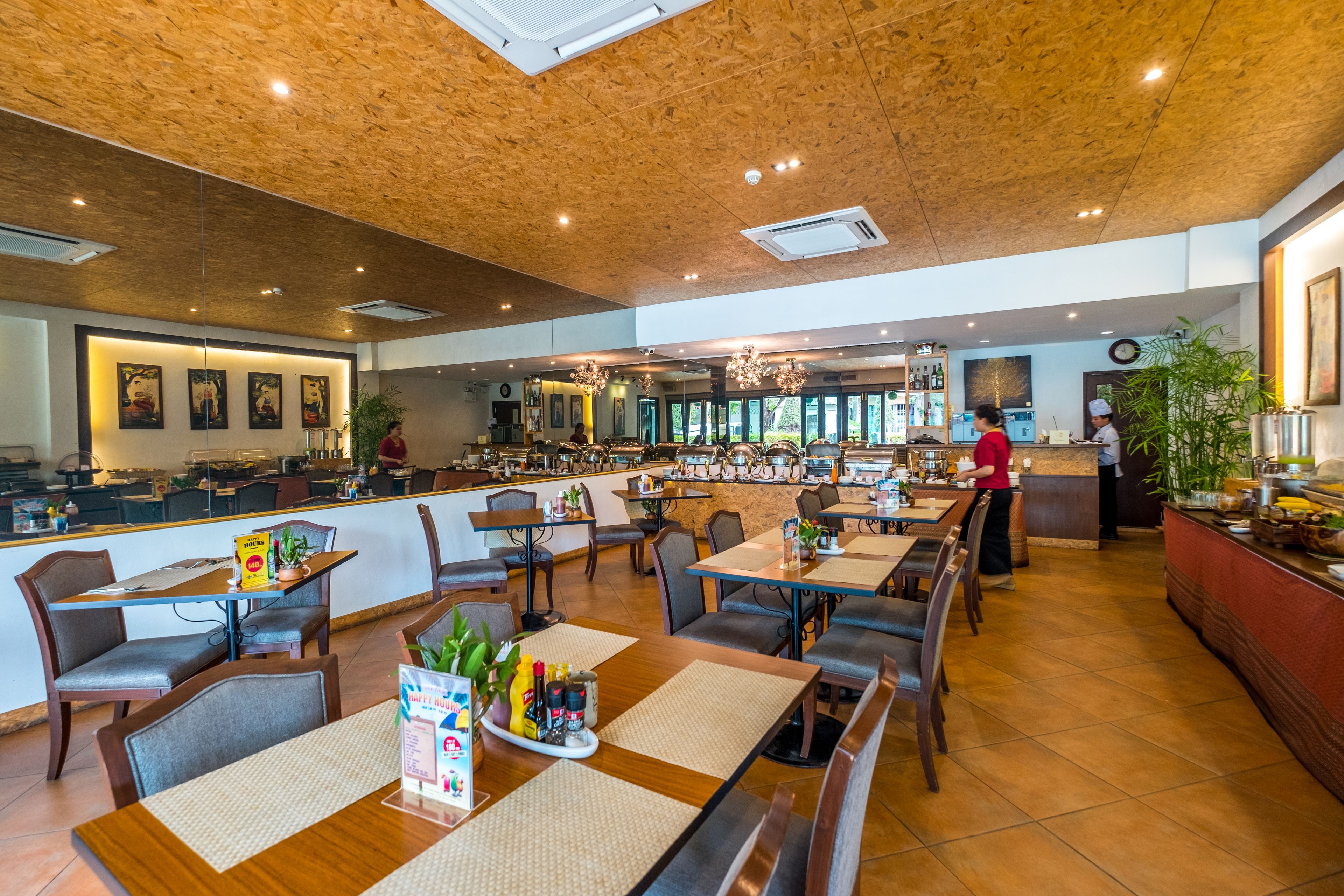 Een ruime restaurantruimte met houten plafond, meerdere eettafels en een bar.