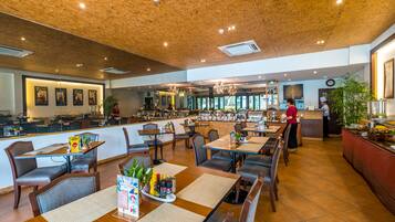 Een ruime restaurantruimte met houten plafond, meerdere eettafels en een bar.