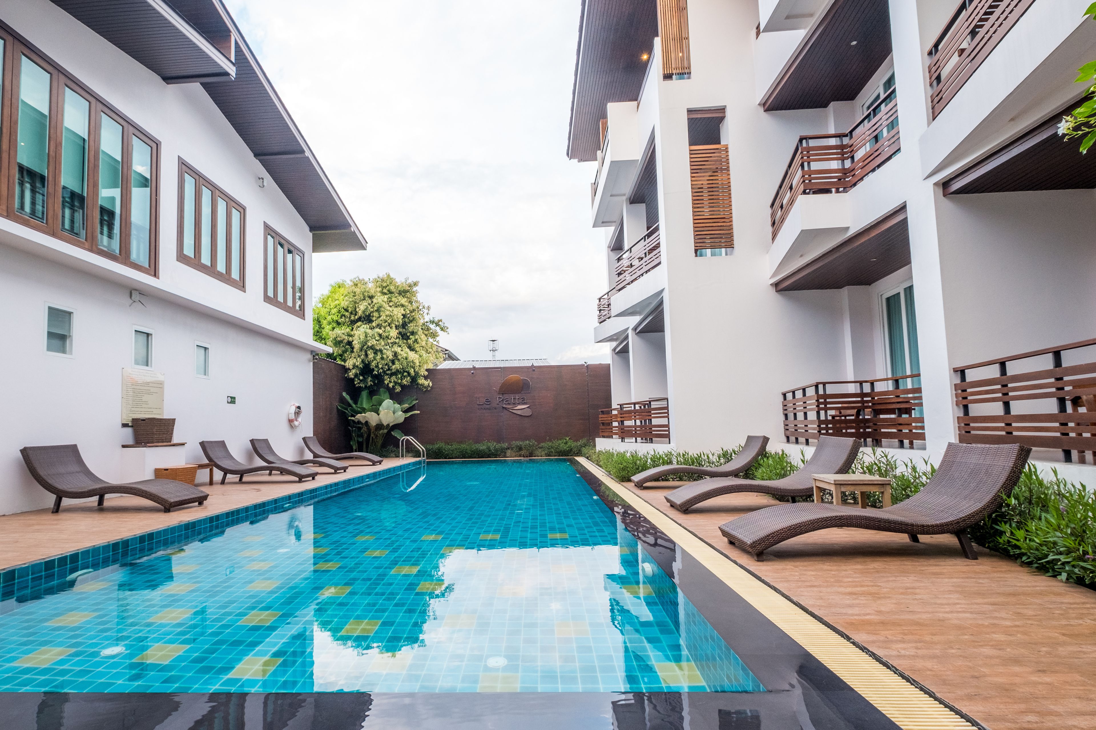 A swimming pool with lounge chairs and a wooden deck, surrounded by modern buildings with balconies.