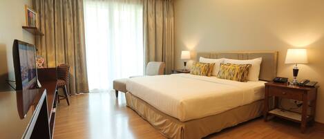 A hotel room with a large bed, two bedside tables with lamps, a TV, a chair, and a large window with curtains.