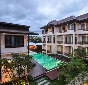A modern hotel with a swimming pool, multiple balconies, and lush greenery.