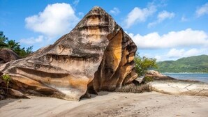 A large rock formation with a cave-like opening, surrounded by sandy beach and greenery. -  Le Vasseur La Buse Eco Resort (Praslin Island)