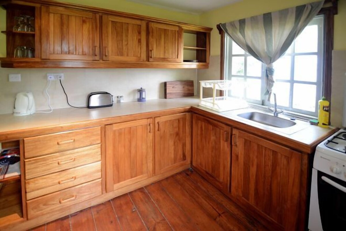 Una cocina con gabinetes de madera, una encimera, un fregadero, una estufa y una ventana con cortinas.