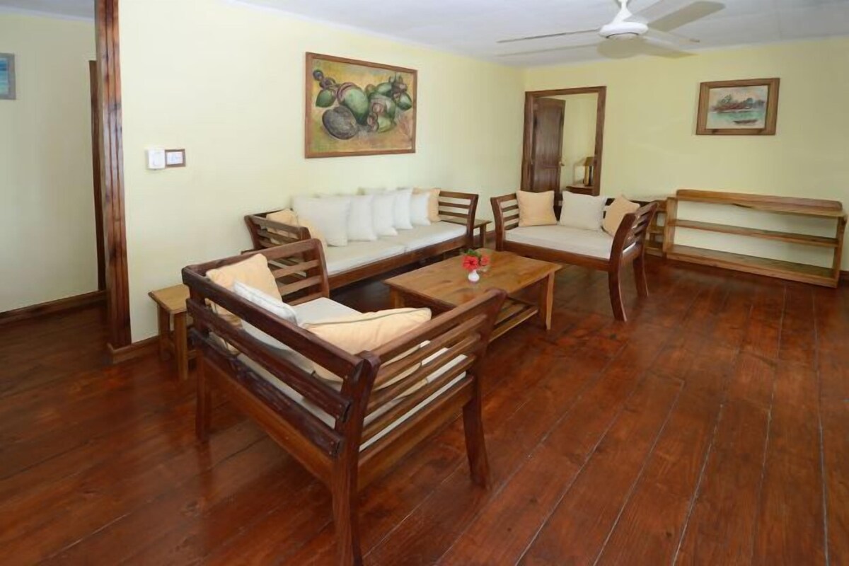 A room with a wooden sofa, a wooden table, and a wooden bench. There are two paintings on the walls.