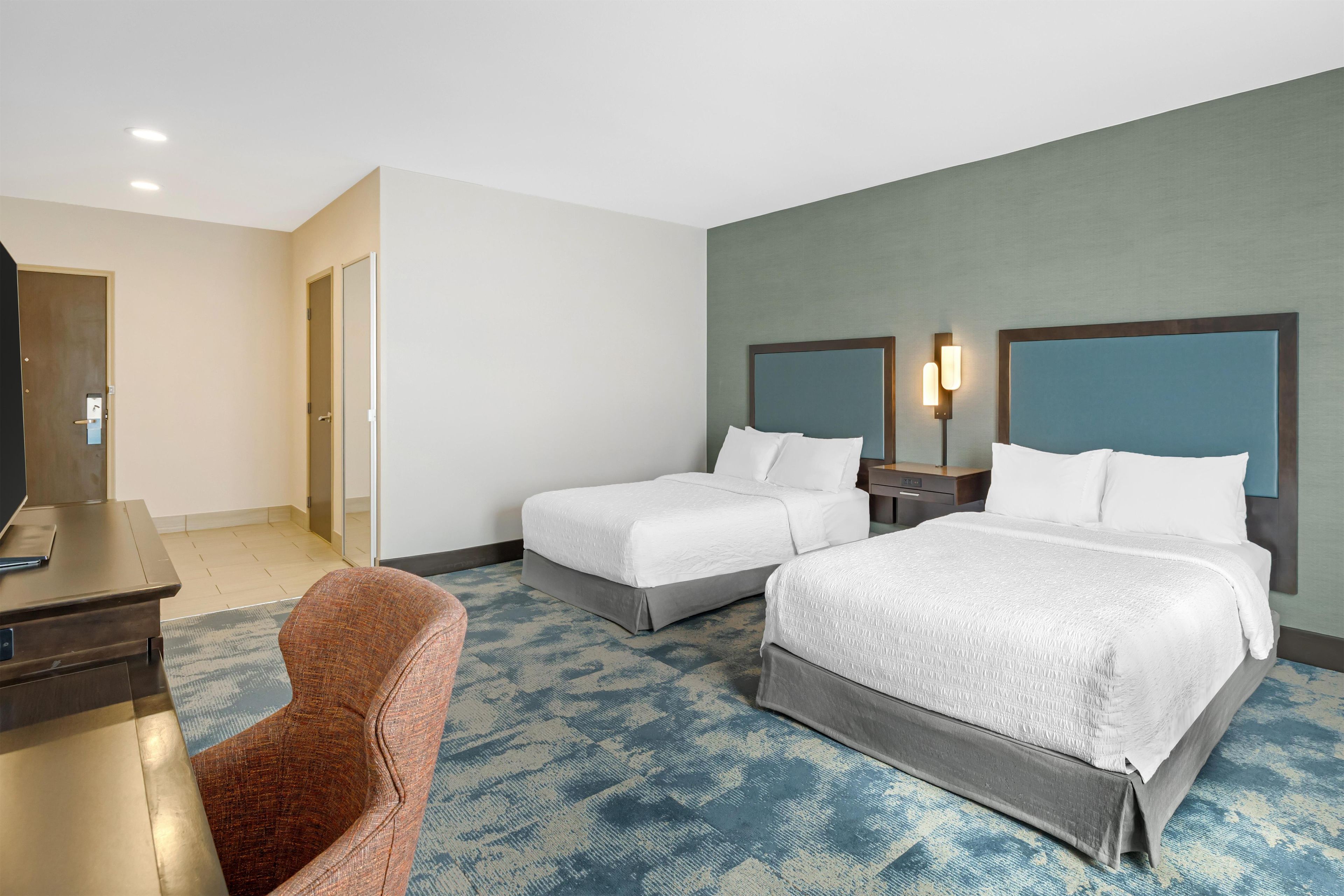 A hotel room with two beds, a desk, a chair, and a television.