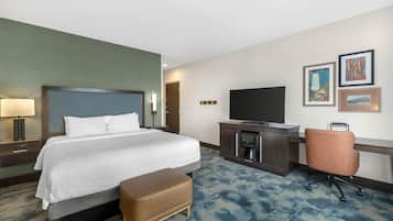 A hotel room with a bed, a desk with a television, a chair, and artwork on the wall.
