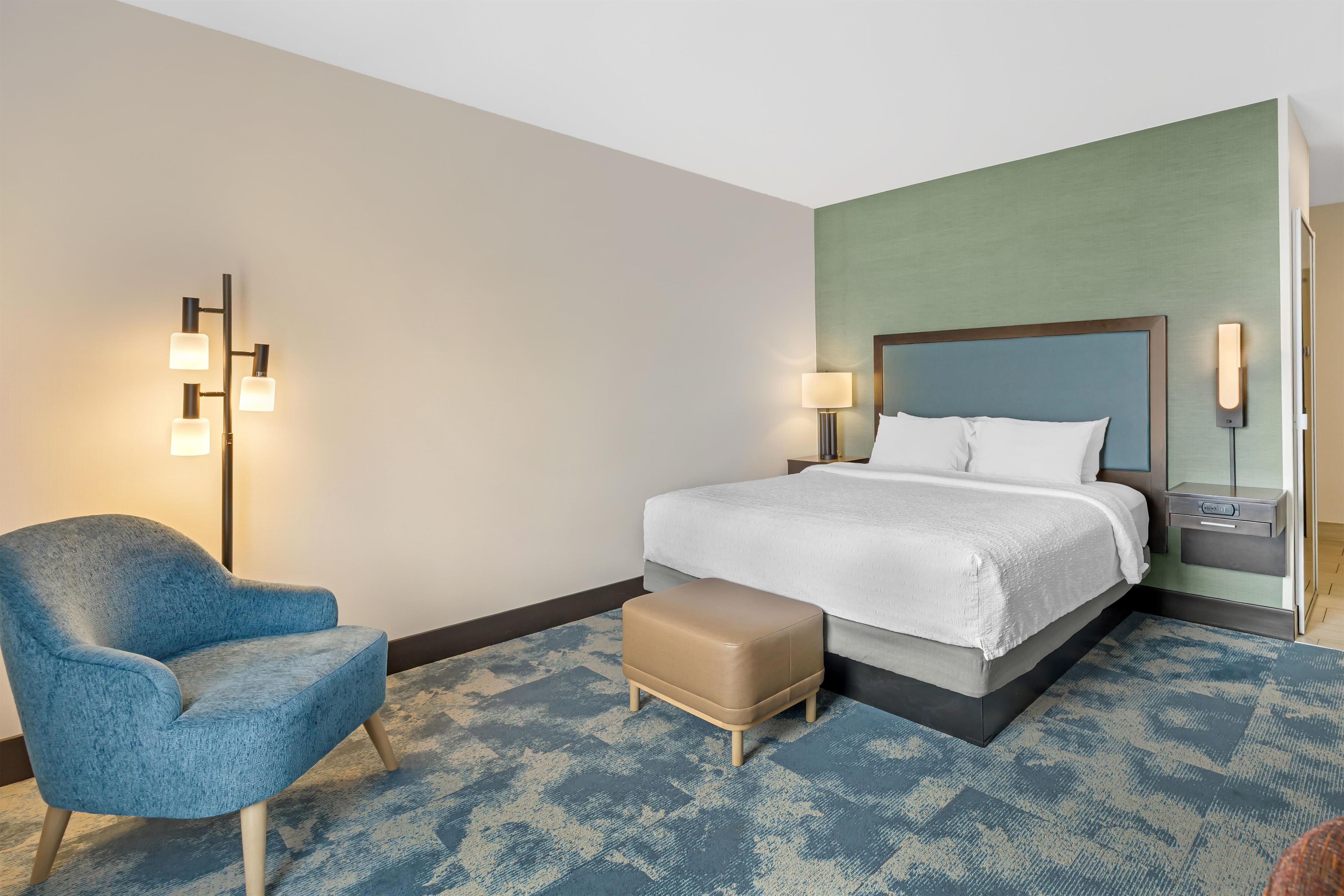 A hotel room with a bed, a chair, a nightstand, and a lamp.