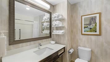 Un baño moderno con un espejo grande, lavabo blanco y inodoro. Hay repisas con toallas y un cuadro en la pared.