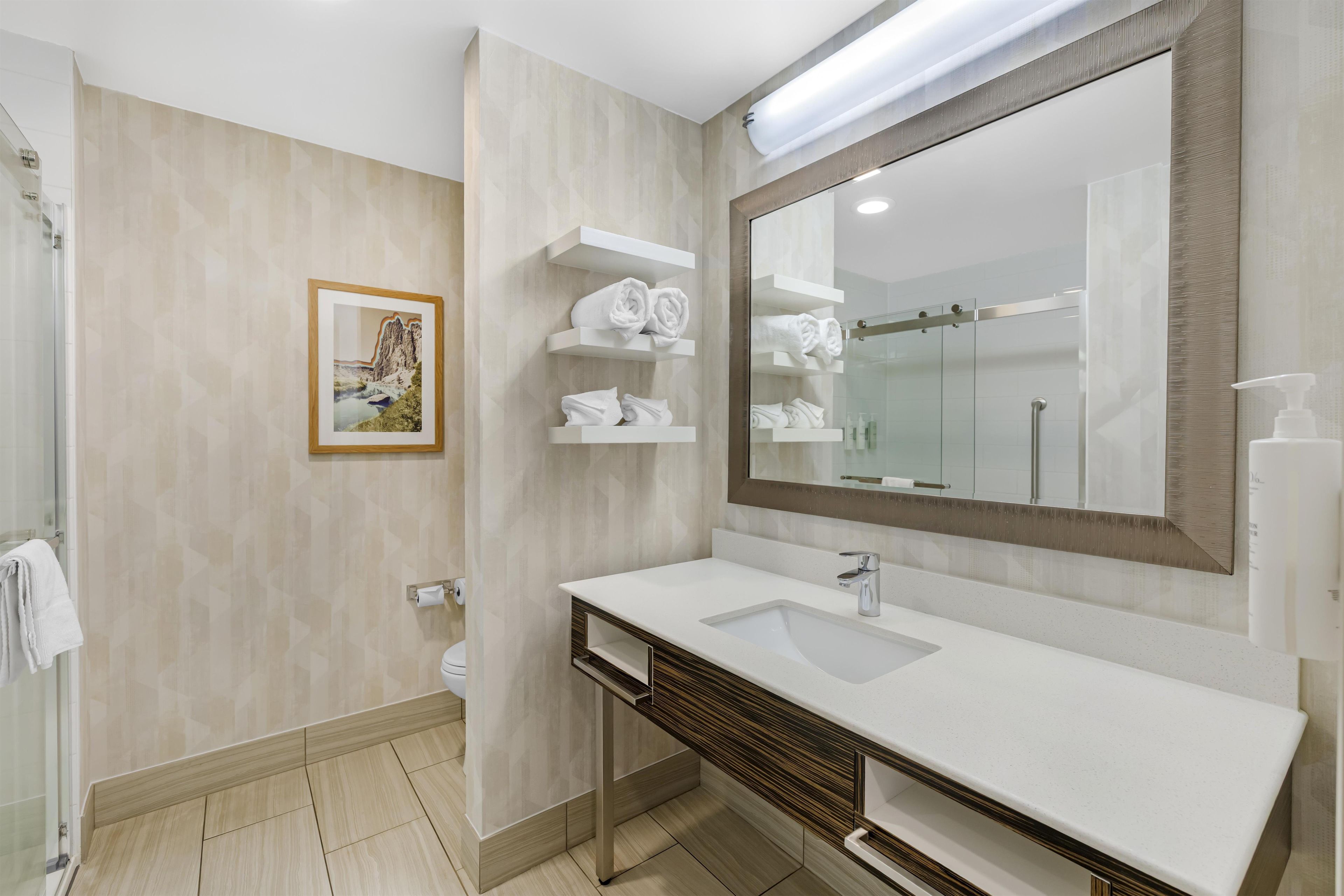 A modern bathroom with a large mirror, white sink, and towel racks.