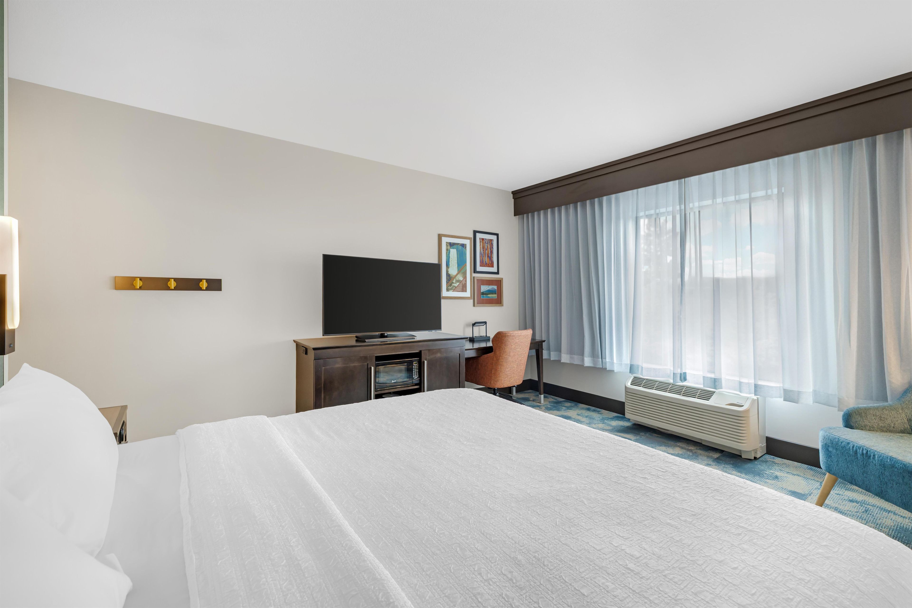 A hotel room with a bed, a desk, a television, a chair, and a window with curtains.