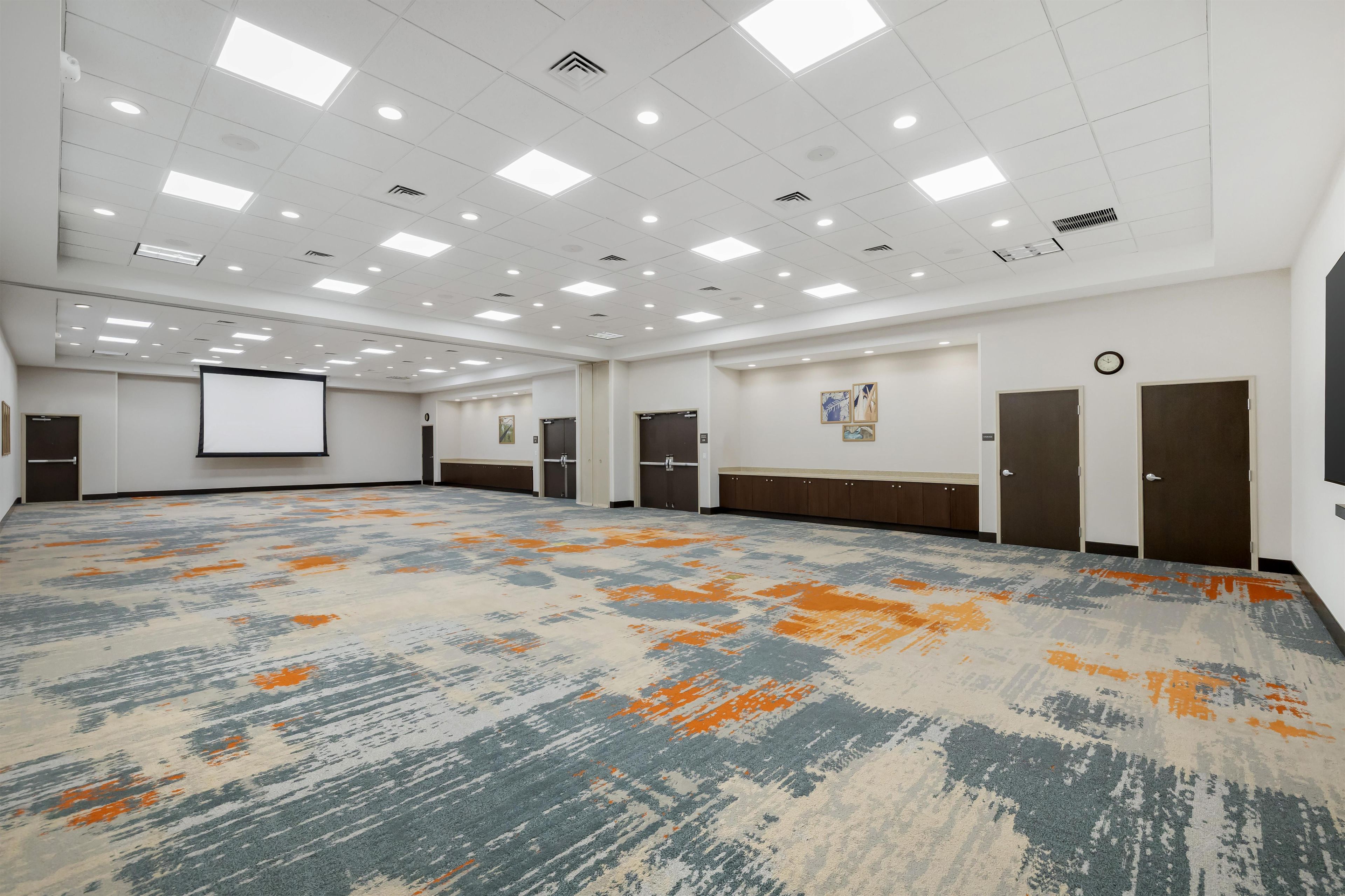 Un salón de conferencias amplio con piso alfombrado, paredes blancas y múltiples luces en el techo.
