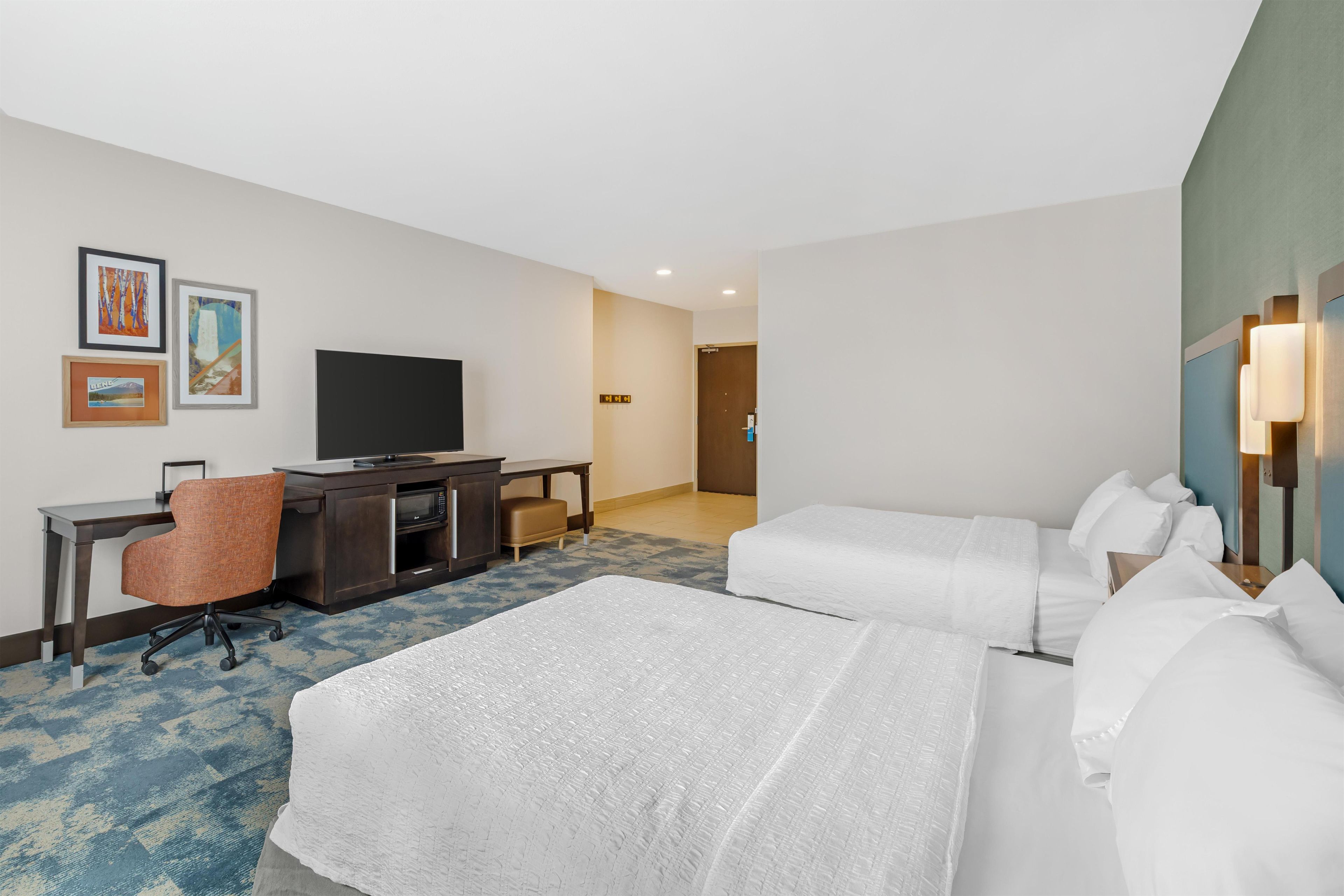 A hotel room with two beds, a desk with a chair, a television, and artwork on the wall.