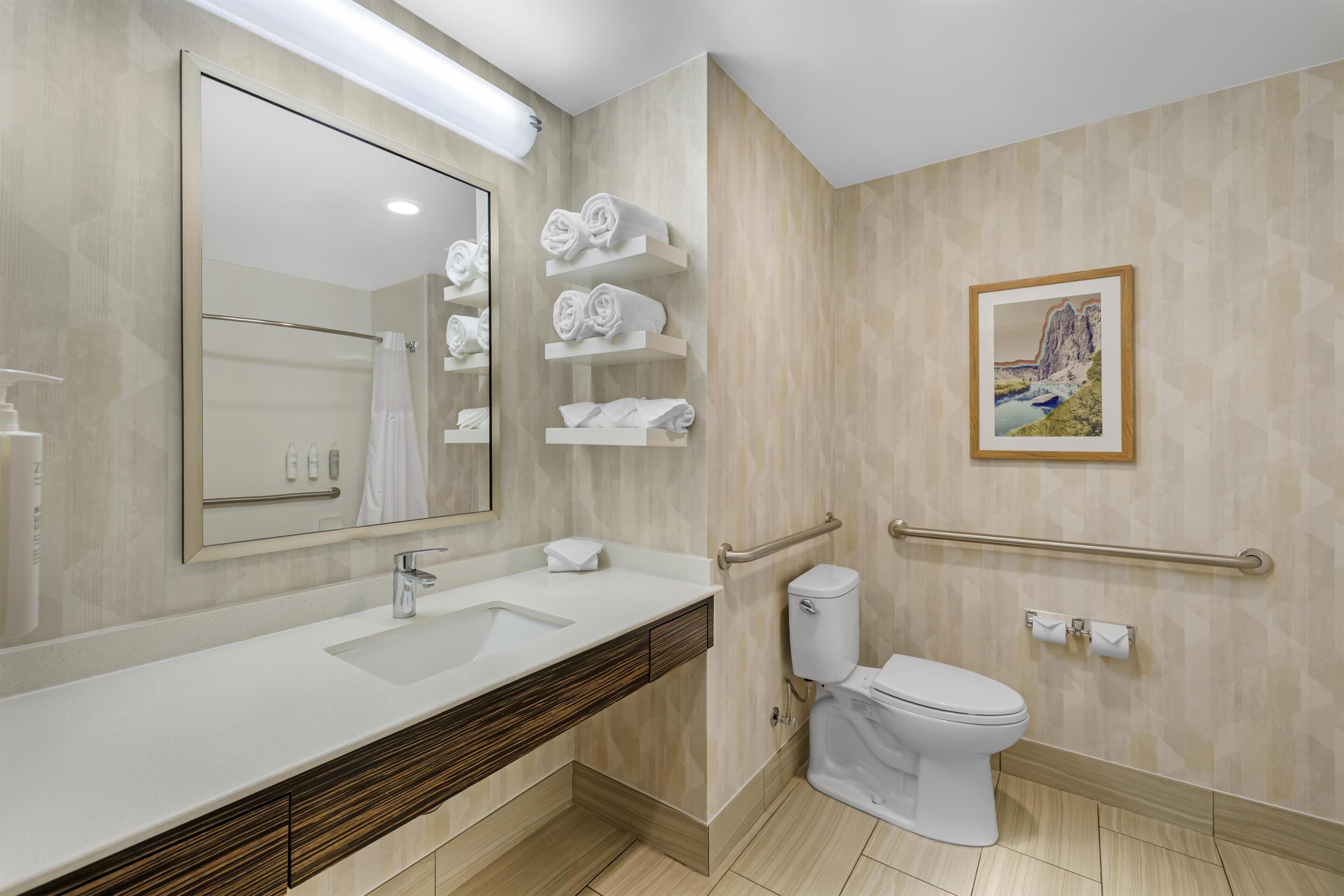 Une salle de bain moderne avec un grand miroir, un lavabo, des toilettes et des porte-serviettes.