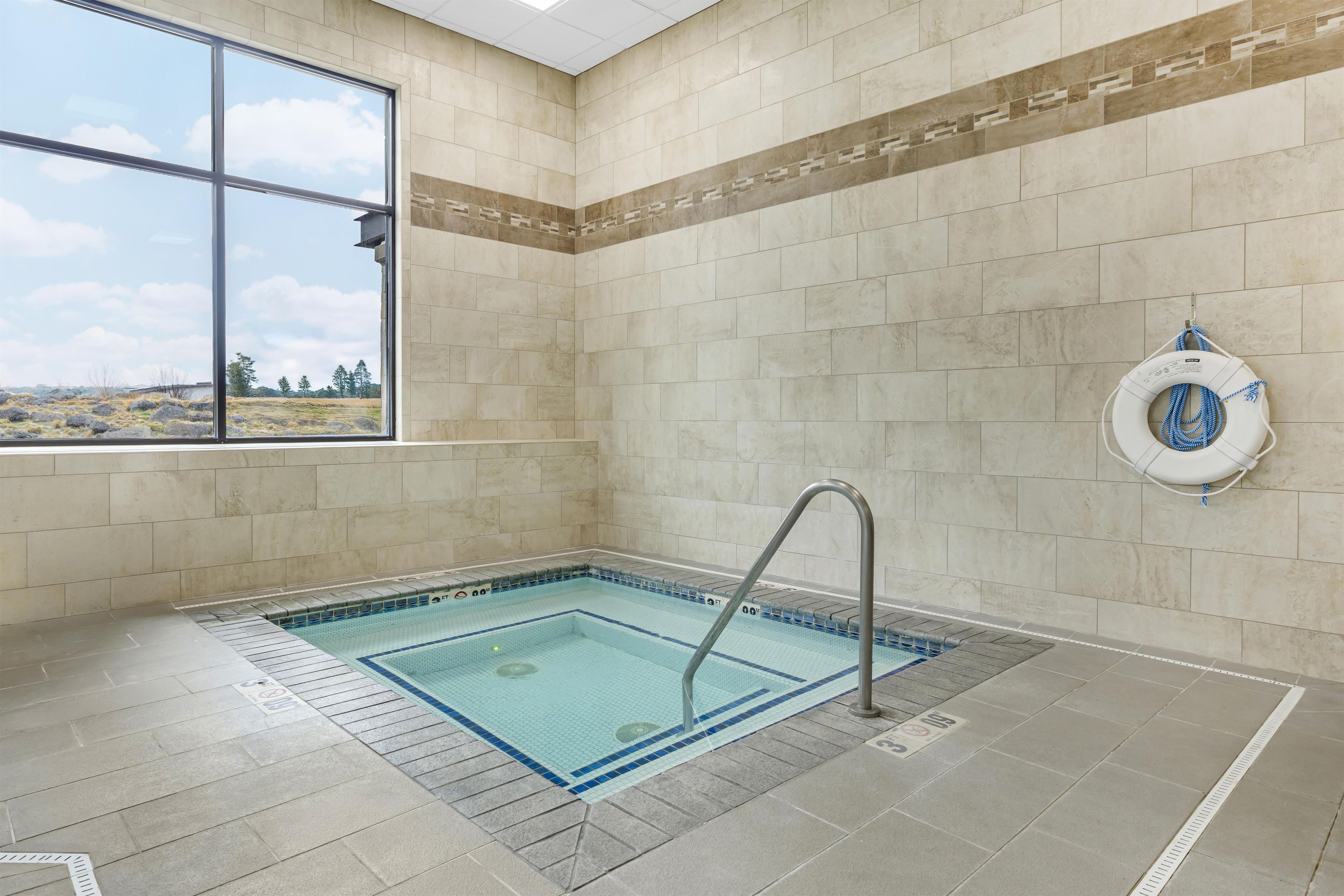 A swimming pool area with a clear view of the outdoors through a large window, a lifebuoy on the wall, and a metal pool ladder.