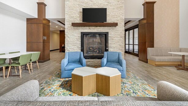 A lobby with a stone fireplace, two blue armchairs, a gray sofa, a wooden coffee table, and a dining area with green chairs. - Hampton Inn & Suites Bend (Bend)