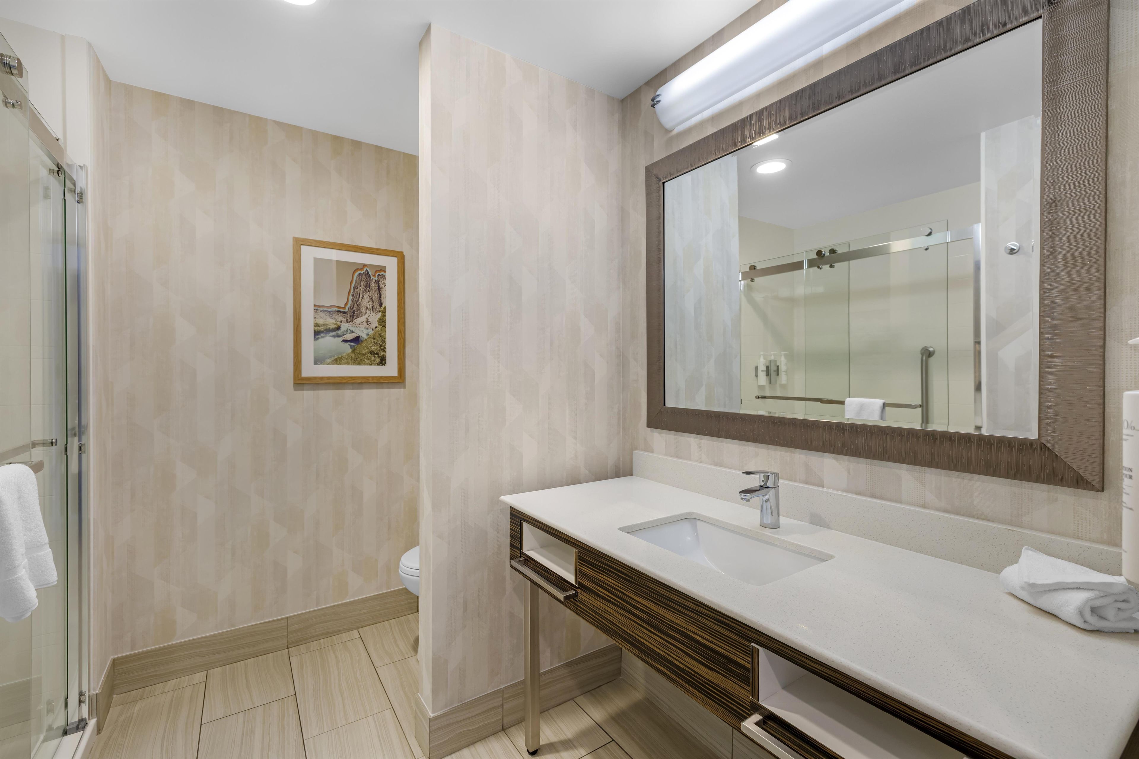 Un baño moderno con un espejo grande, un lavamanos y una ducha.
